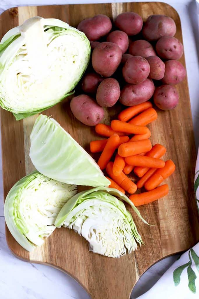Cabbage wedges, small potatoes and baby carrots on a wooden board.