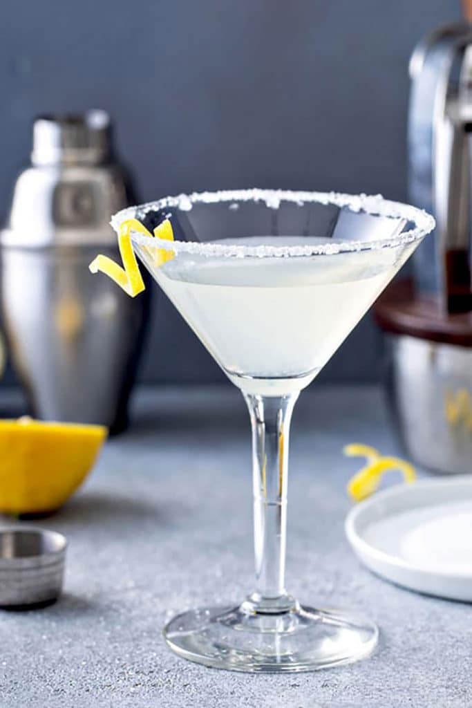 A martini glass with lemon drop martini cocktail and a lemon twist on a gray counter