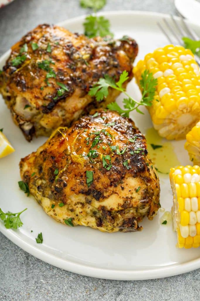 Two baked crispy chicken thighs served with buttered corn.