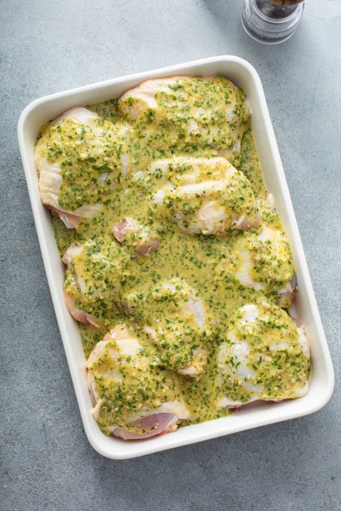 Skin on chicken thighs marinating in a white dish.