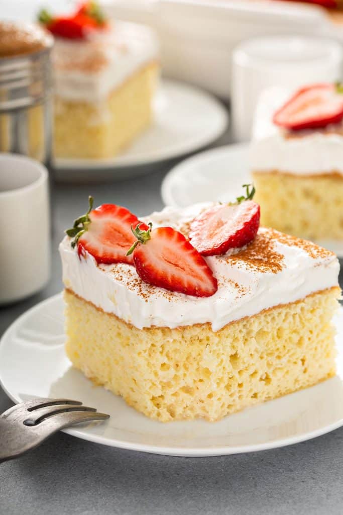 moist tres leches cake on plate with frosting and strawberry halves