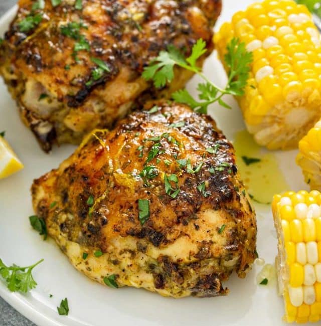Two baked crispy chicken thighs served with buttered corn.