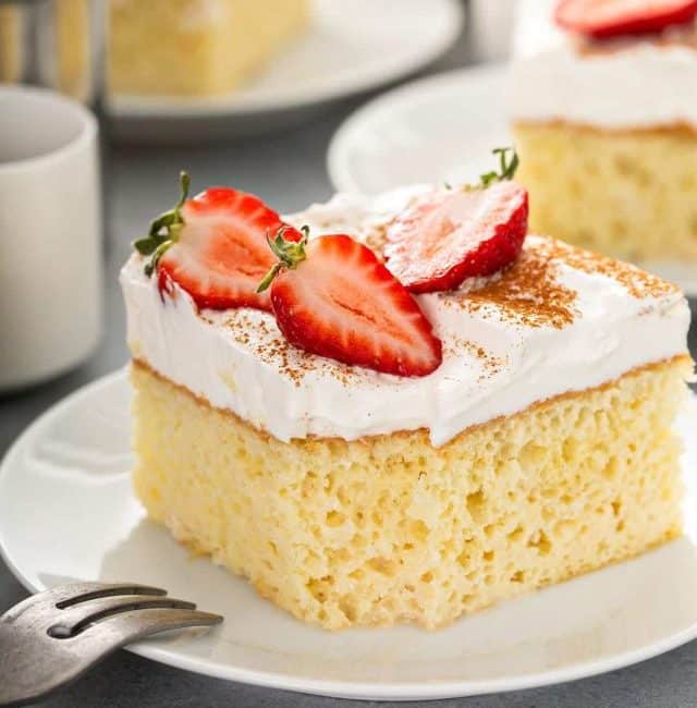 moist tres leches cake on plate with frosting and strawberry halves