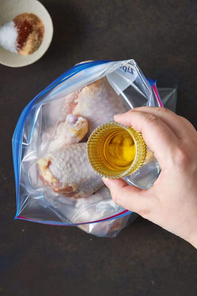 Pouring oil over raw chicken legs