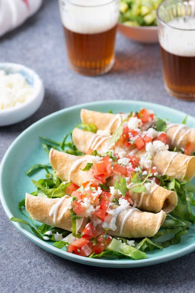 Crispy taquitos topped with crumbled cheese, tomatoes and cilantro