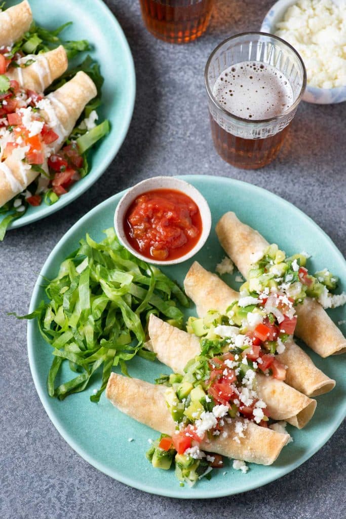Crispy taquitos with assorted toppings on a plate