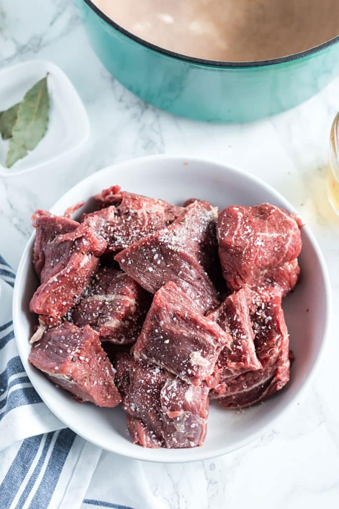 big chunks of beef seasoned with salt and pepper in a white bowl