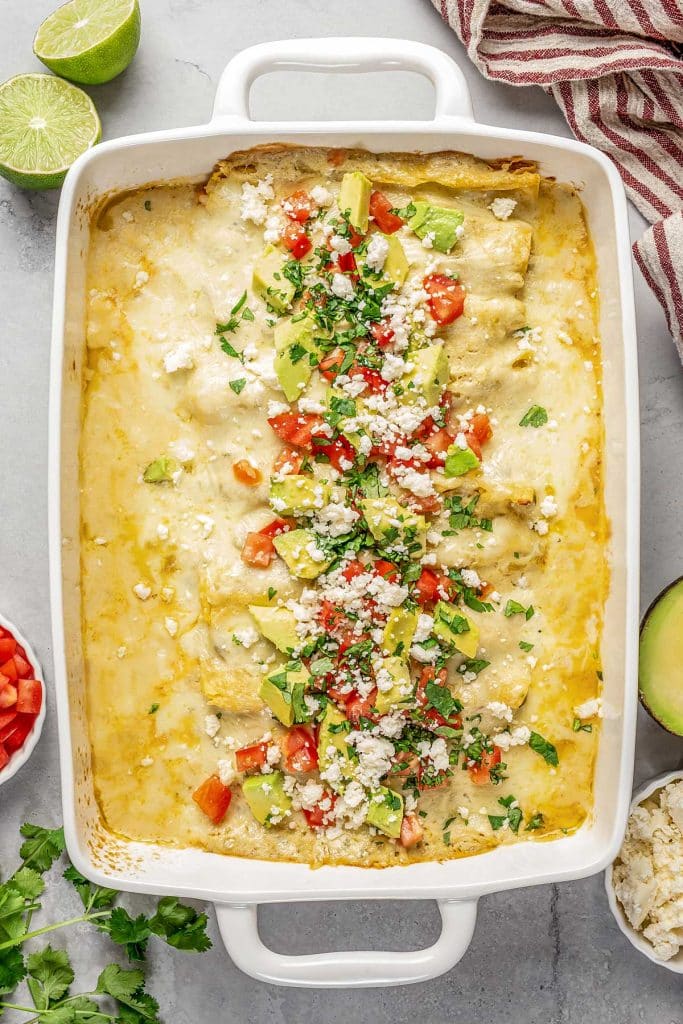 Top view of shrimp enchilada in a baking dish topped with cheese, diced tomatoes and avocados.