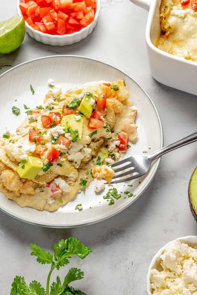 enchiladas topped with cheese, tomatoes and avocado on plate with fork
