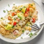 enchiladas topped with cheese, tomatoes and avocado on plate with fork