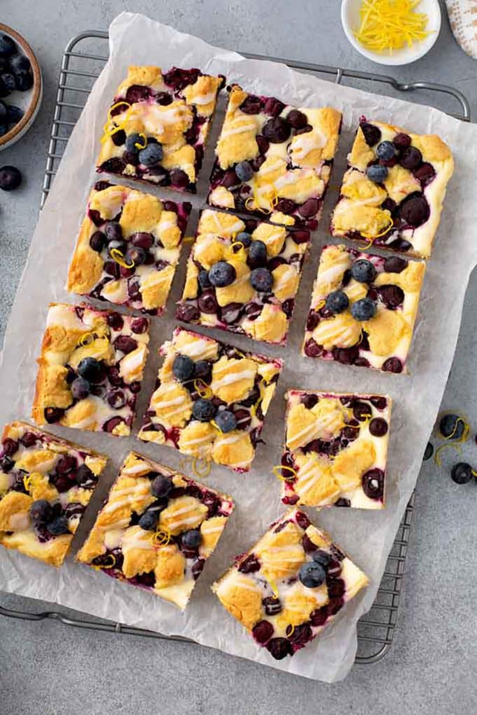 Cut up cheesecake crumb bars with blueberries on parchment paper.