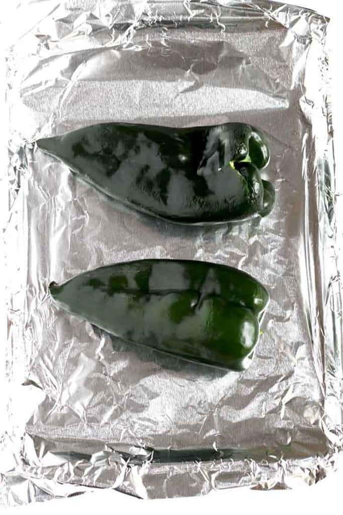 two poblano peppers on a sheet pan with aluminium foil