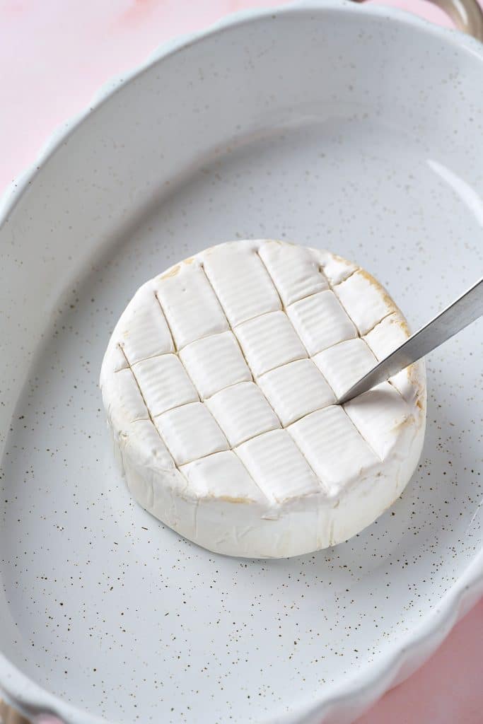 lightly cutting the top of the brie wheel with a knife 