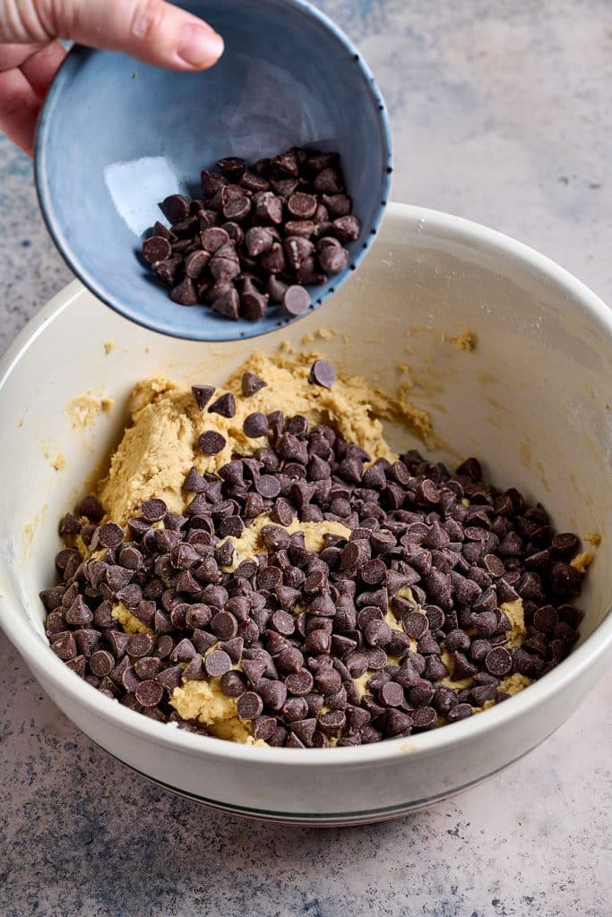 pouring chocolate chips onto the cookie dough