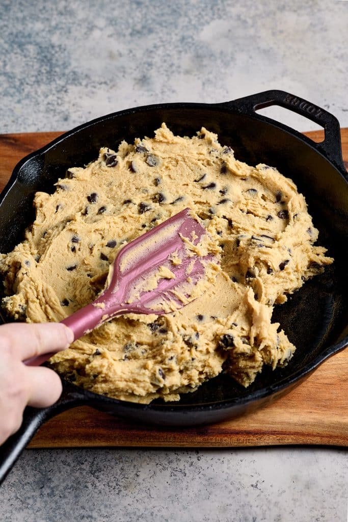 spreading the chocolate chip cookie dough into a skillet.