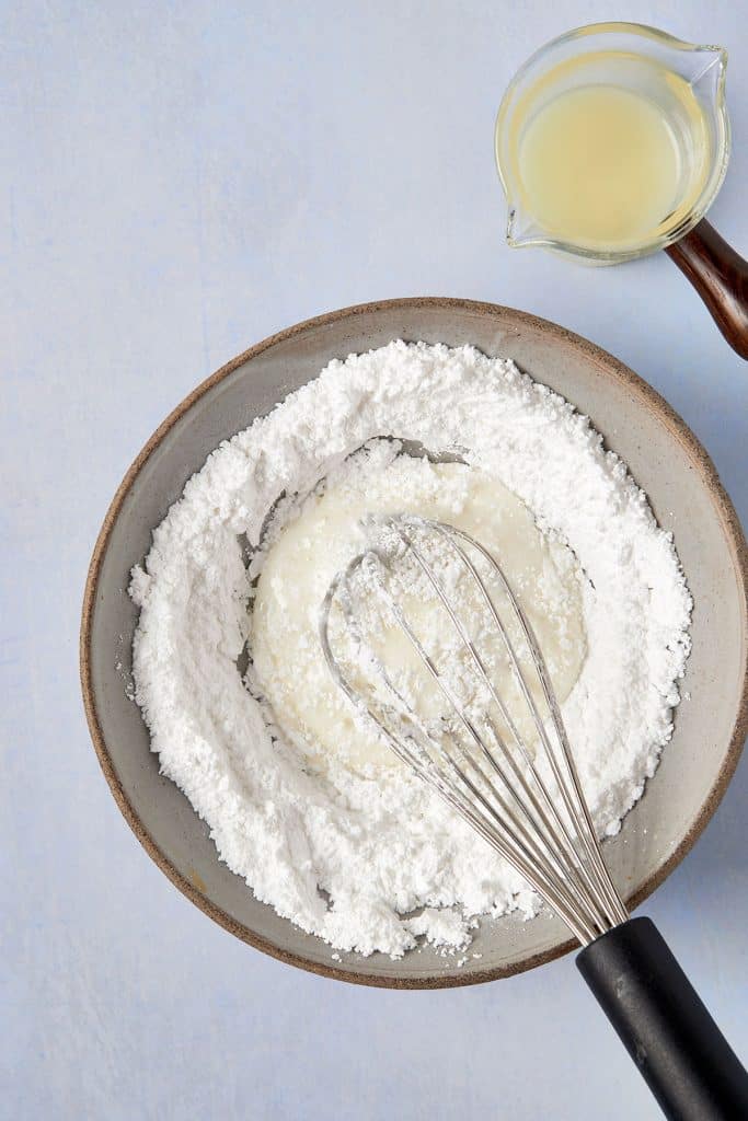 A bowl with powdered sugar, lemon juice and a whisk