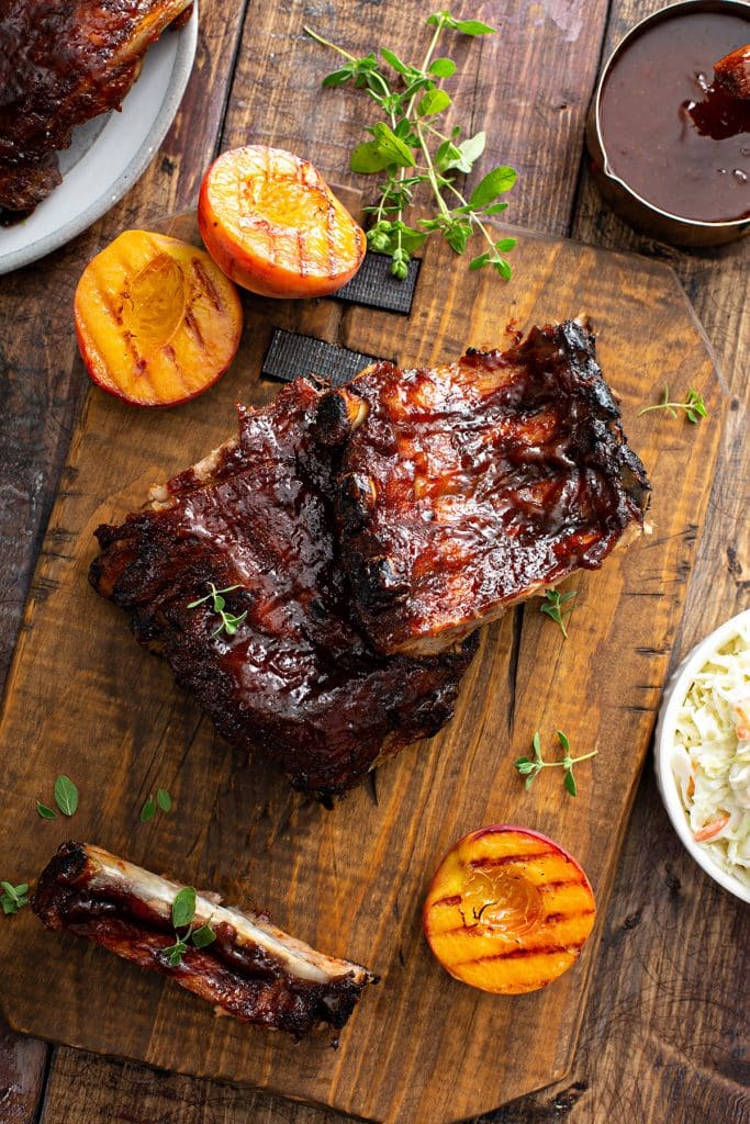 A wooden board with tender bbq ribs, and grilled peaches