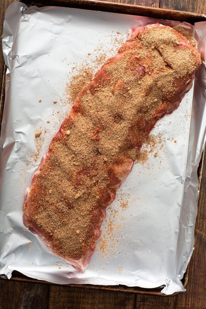 A slab of ribs rubbed with dried spices on a sheet pan