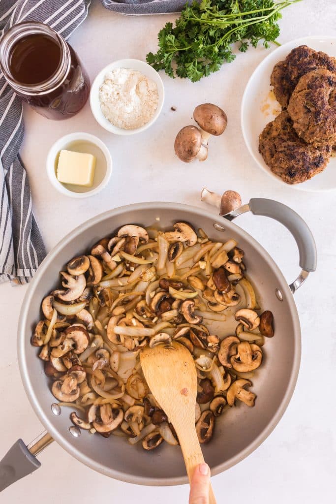 Stirring sautéed onions and mushrooms in a skillet
