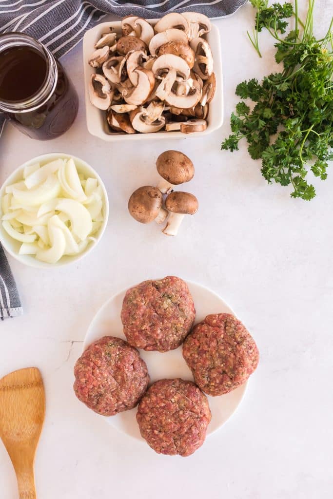 Meat patties on a plate, raw onions and mushrooms  
