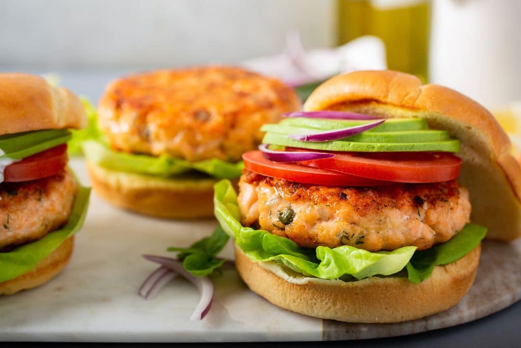 Salmon Burgers on brioche buns topped with tomato slices, red onions and avocado.