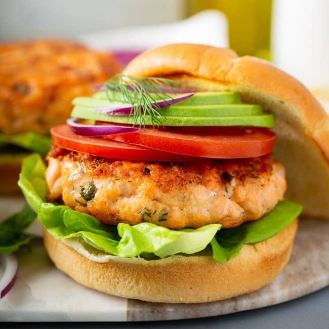 Salmon Burger on top of a brioche bun topped with sliced tomatoes, onions and avocado