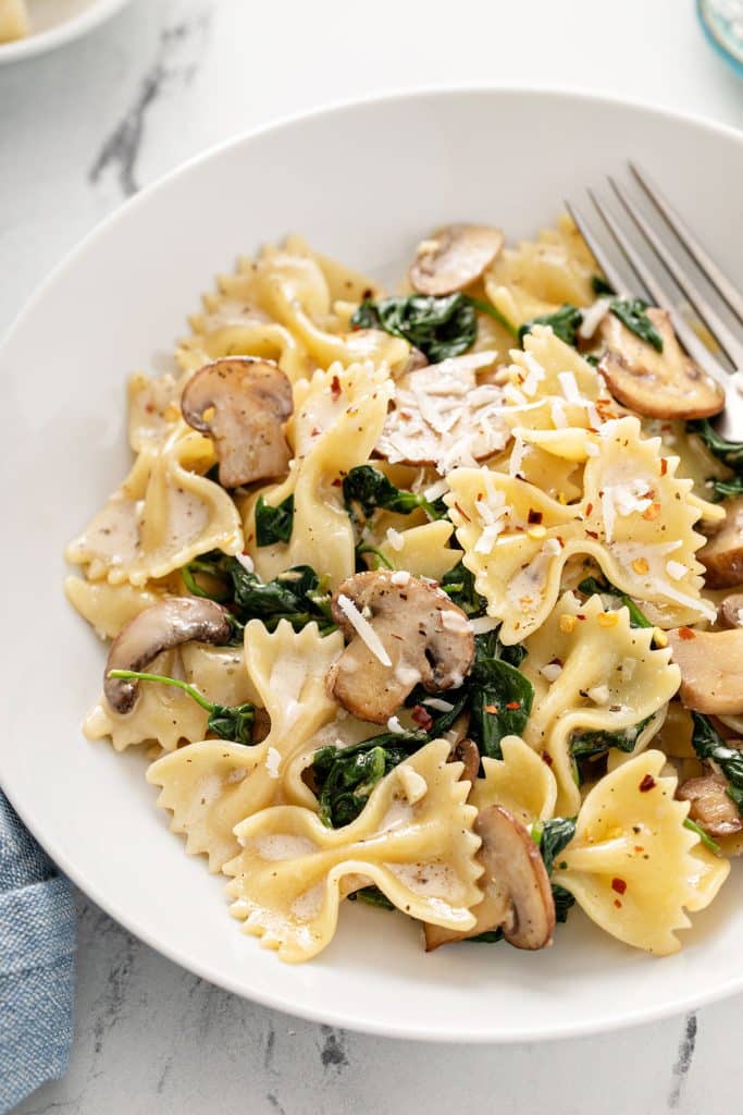 Farfalle pasta with spinach and mushrooms in a white bowl