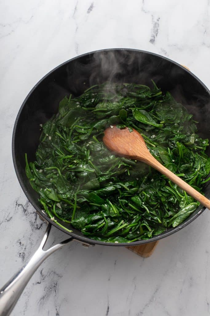 Spinach sautéing in a large skillet