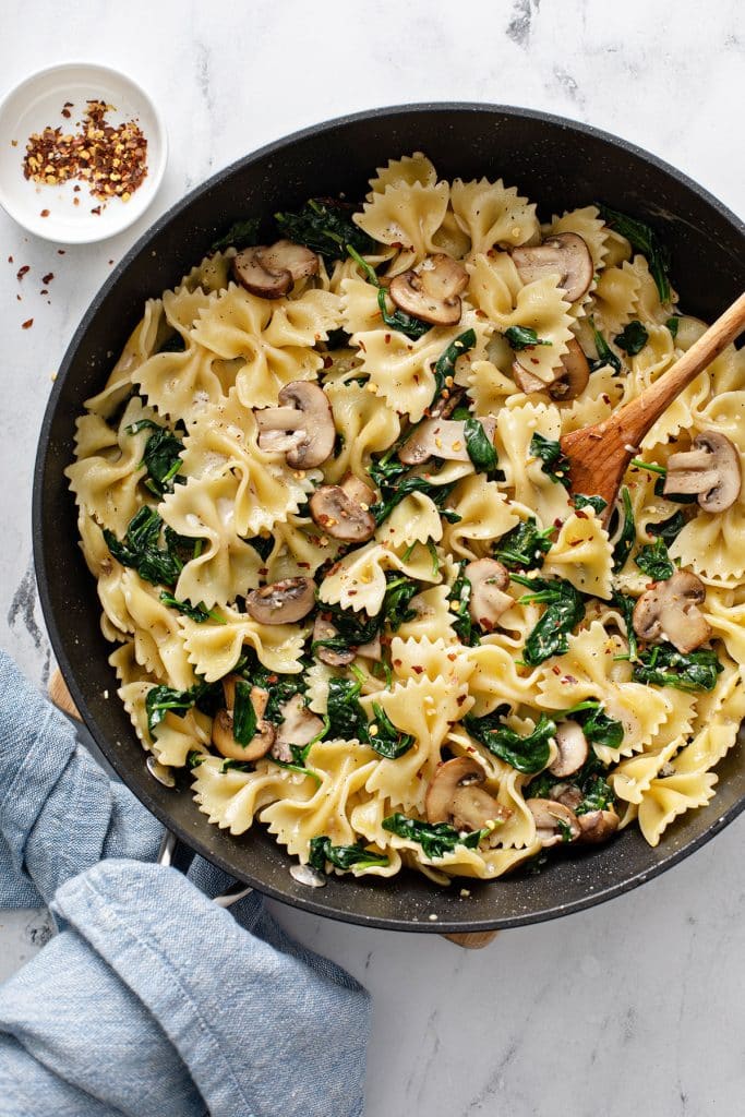 Bow tie pasta with sautéed  mushrooms and spinach in a skillet