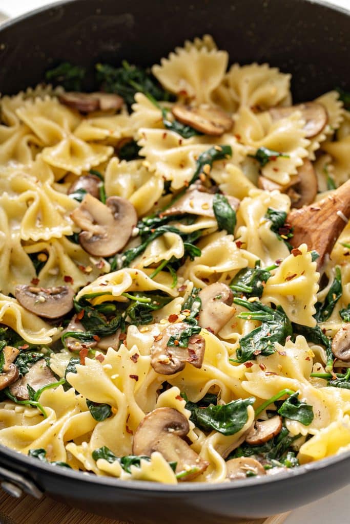 Close up view of farfalle with sautéed onions, spinach, garlic and red pepper flakes in a skillet