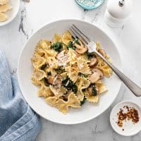 Farfalle, mushrooms and spinach in a white bowl