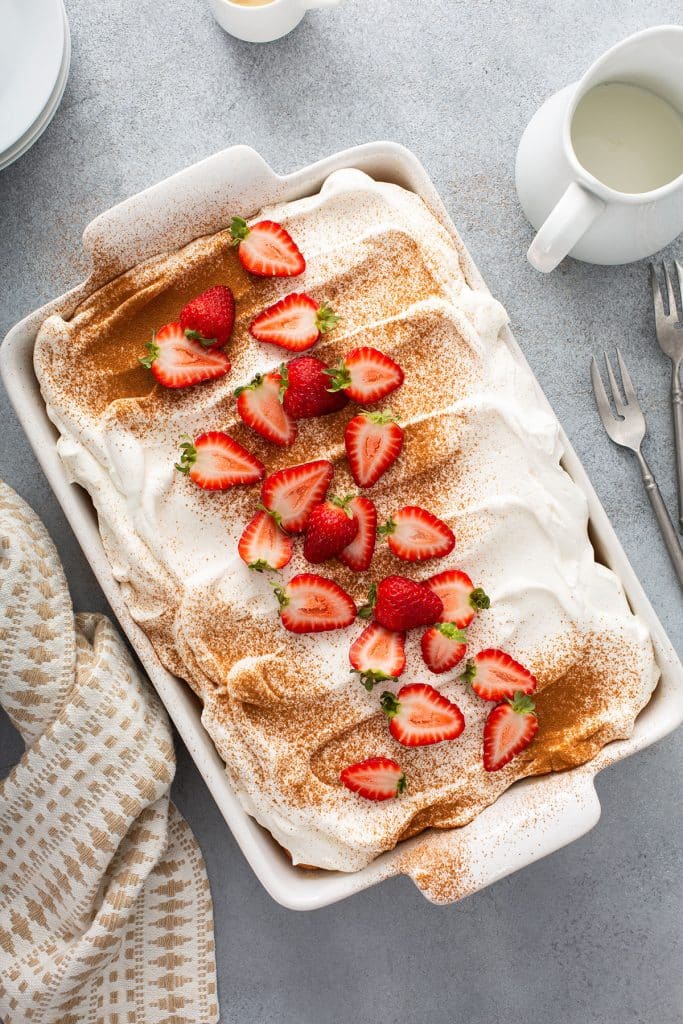 Cake topped with whipped cream frosting, dusted with cinnamon and garnished with strawberries in a rectangular cake pan