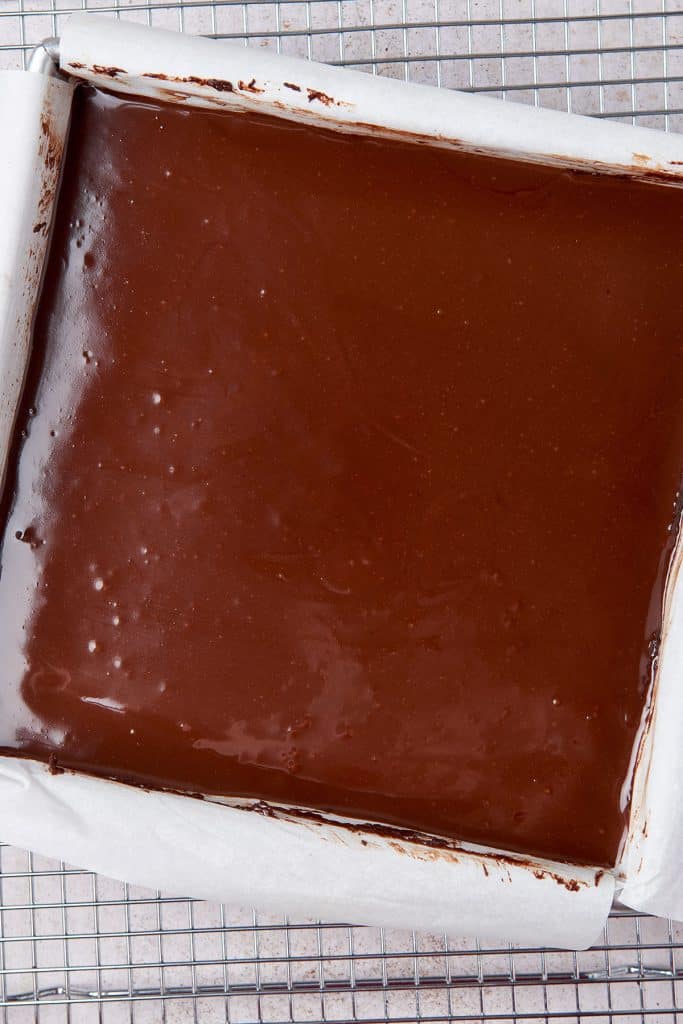 Smooth and shiny chocolate ganache on top of brownie in a pan