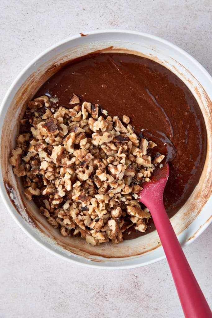 Chopped walnuts added to a bowl filled with chocolate batter
