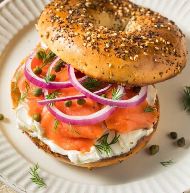 Toasted everything bagel topped with cream cheese, sliced red onion and capers on a plate
