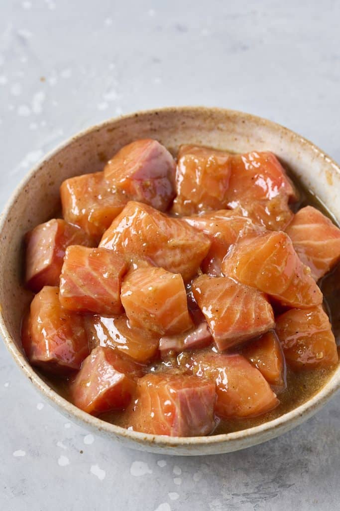 Raw salmon cut into small nuggets marinating in a bowl