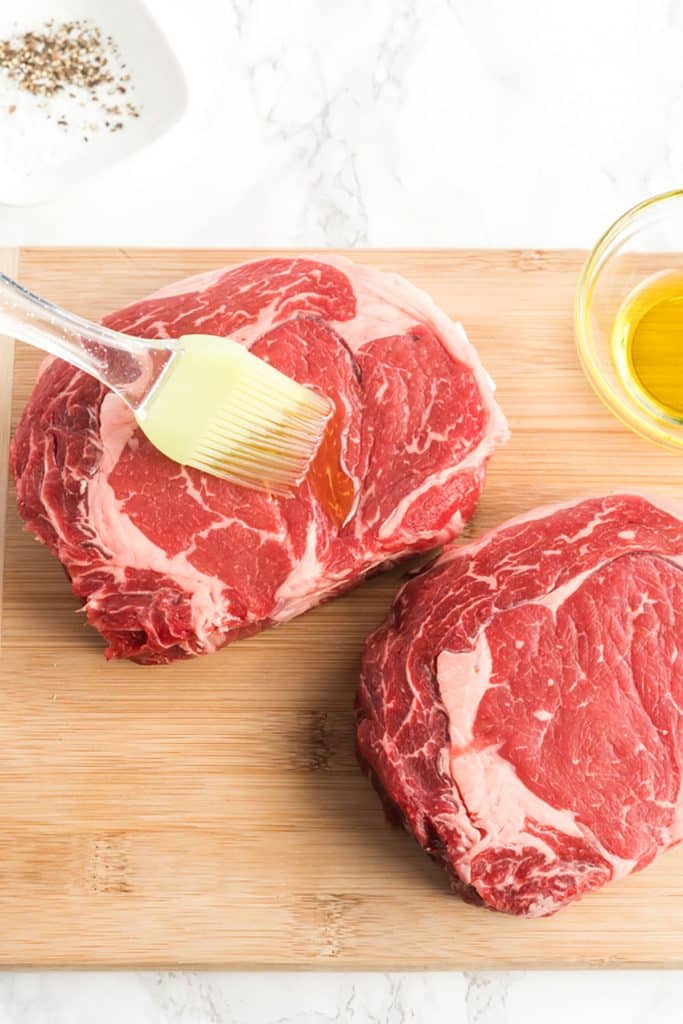 spreading oil over a ribeye steak with a brush