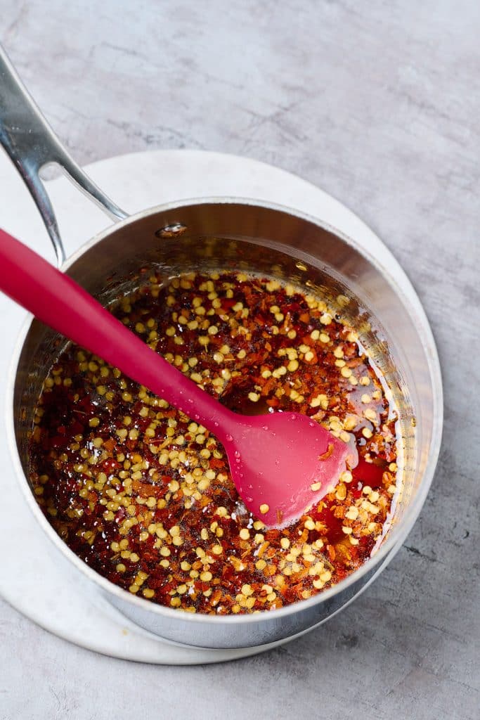 simmering honey with chili flakes in a saucepan with a red spatula