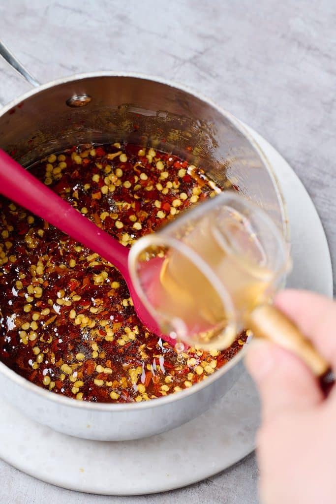 pouring apple cider vinegar into the hot honey sauce