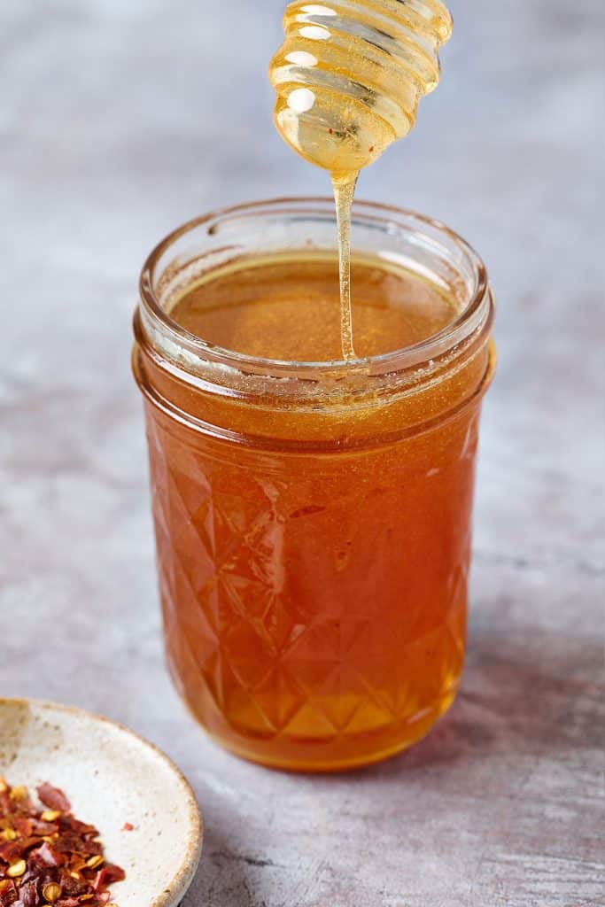 close up of honey honey drizzling from a dipper into a jar