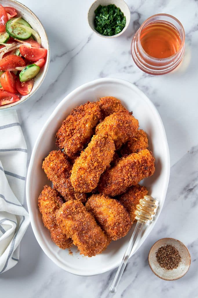 crispy chicken in a bowl with side salad and jar of hot honey