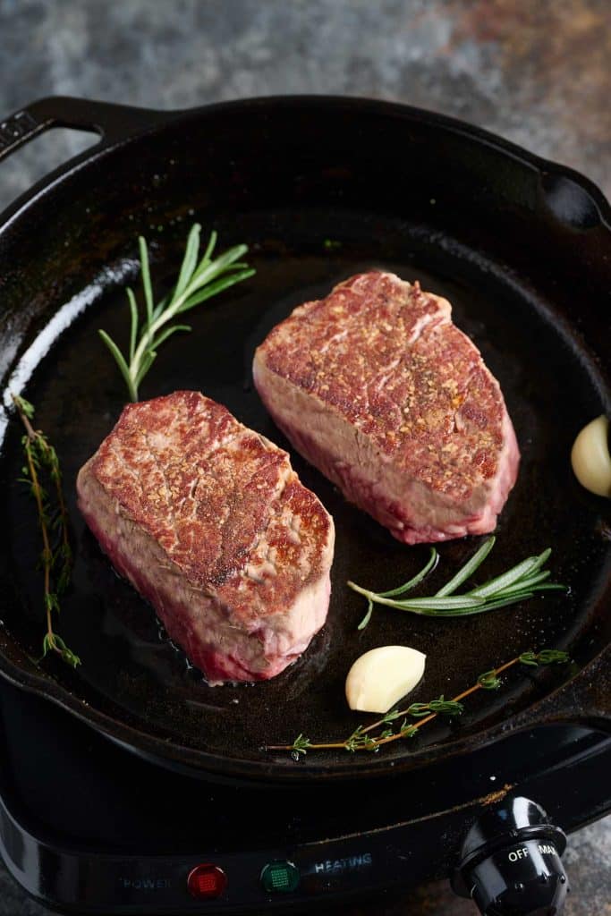 Golden brown steaks in a skillet with garlic, rosemary and thyme