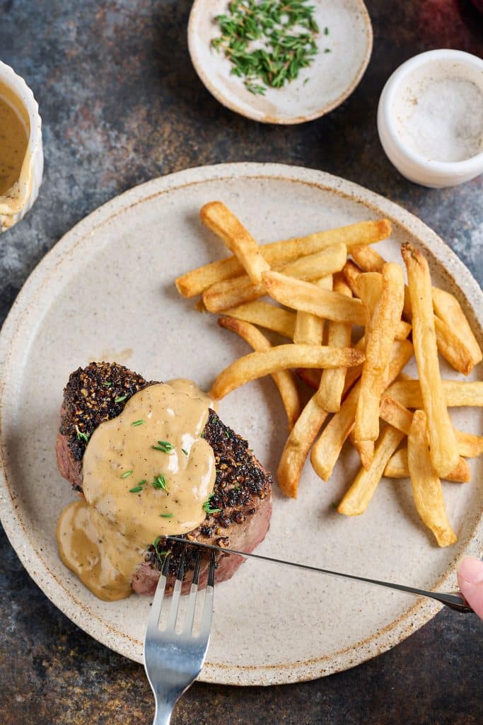 cutting steak au poivre on a plate with french fries
