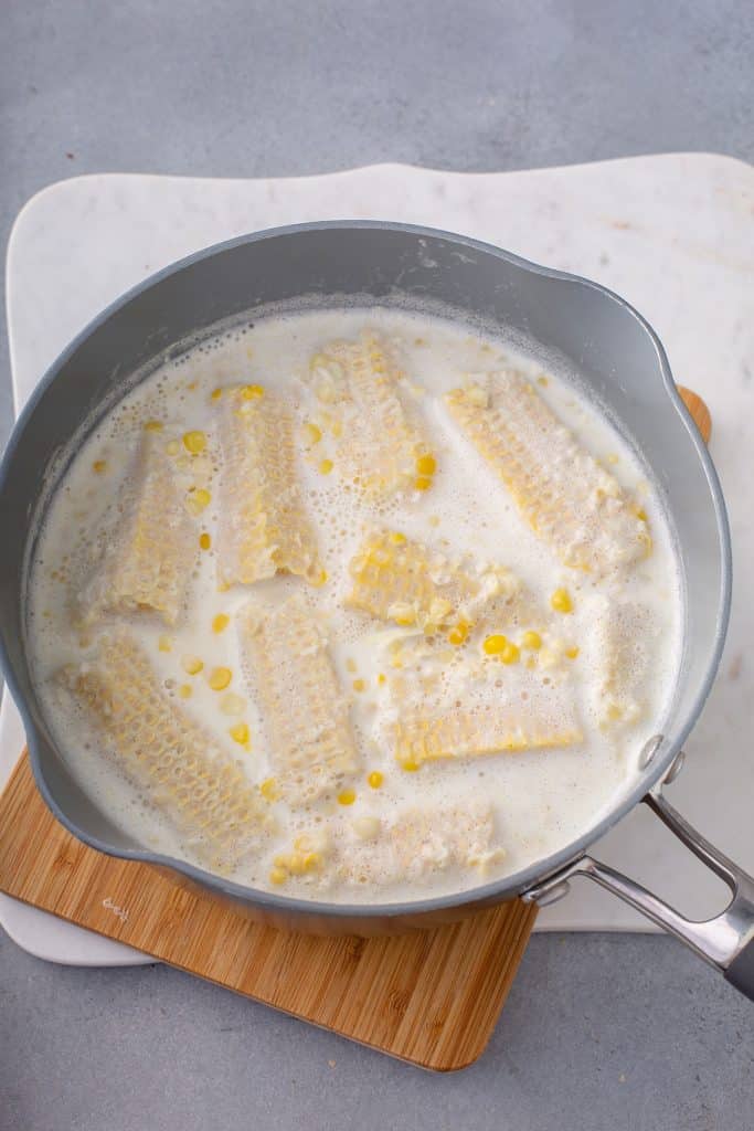 corn cobs simmering in milk, cream and sugar