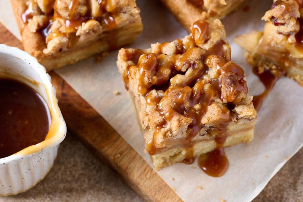 top view of apple pie bars with a pecan crumble and drizzled with salted caramel sitting on a piece of parchment paper.