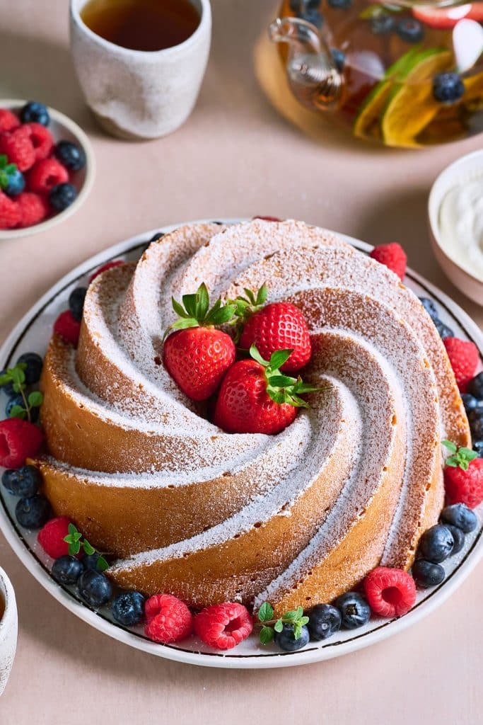 A whole bundt cake dusted with powdered sugar and served with berries