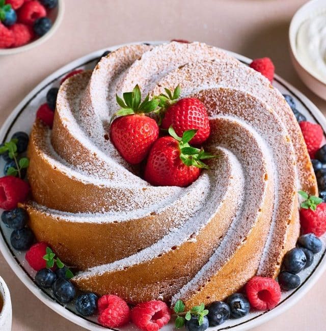 A whole bundt cake dusted with powdered sugar and served with berries