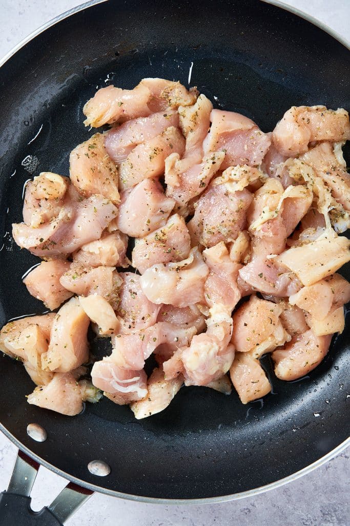 Seasoned raw chicken breast pieces in a skillet