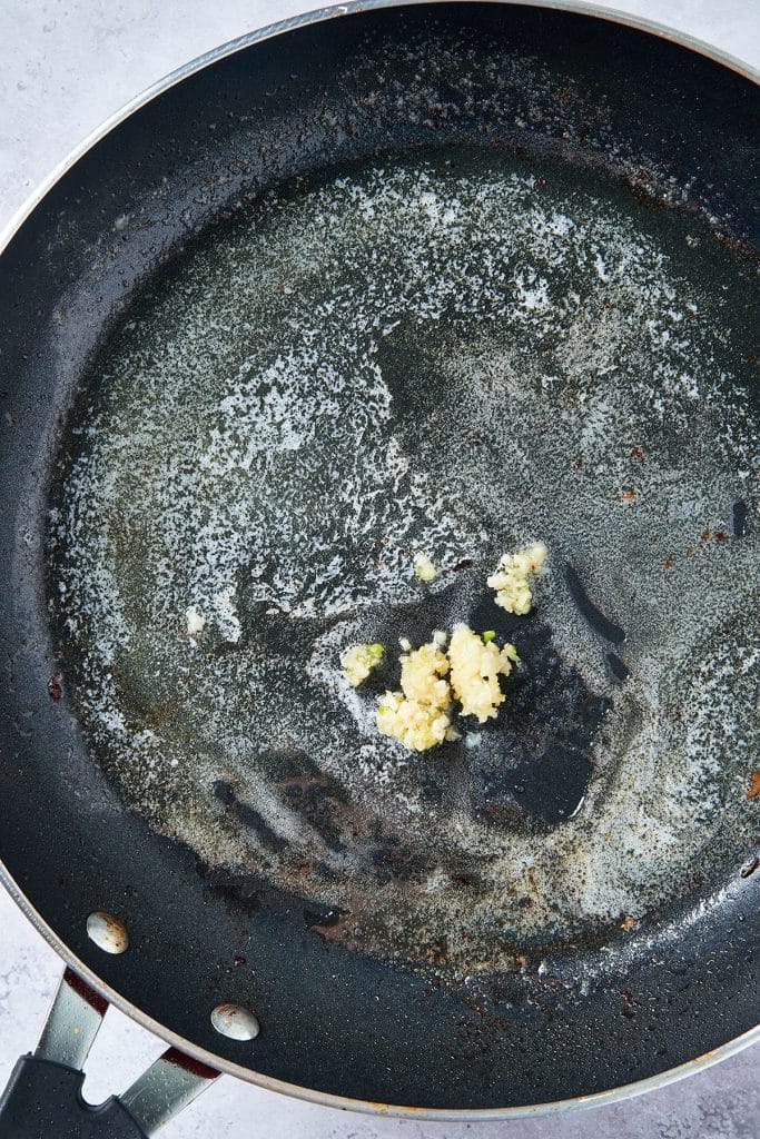 Minced garlic cooking in butter in a skillet.