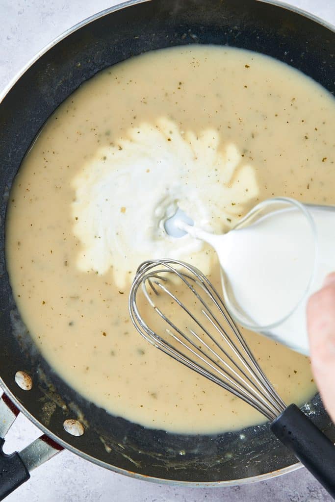 Pouring half and half in a skillet with sauce